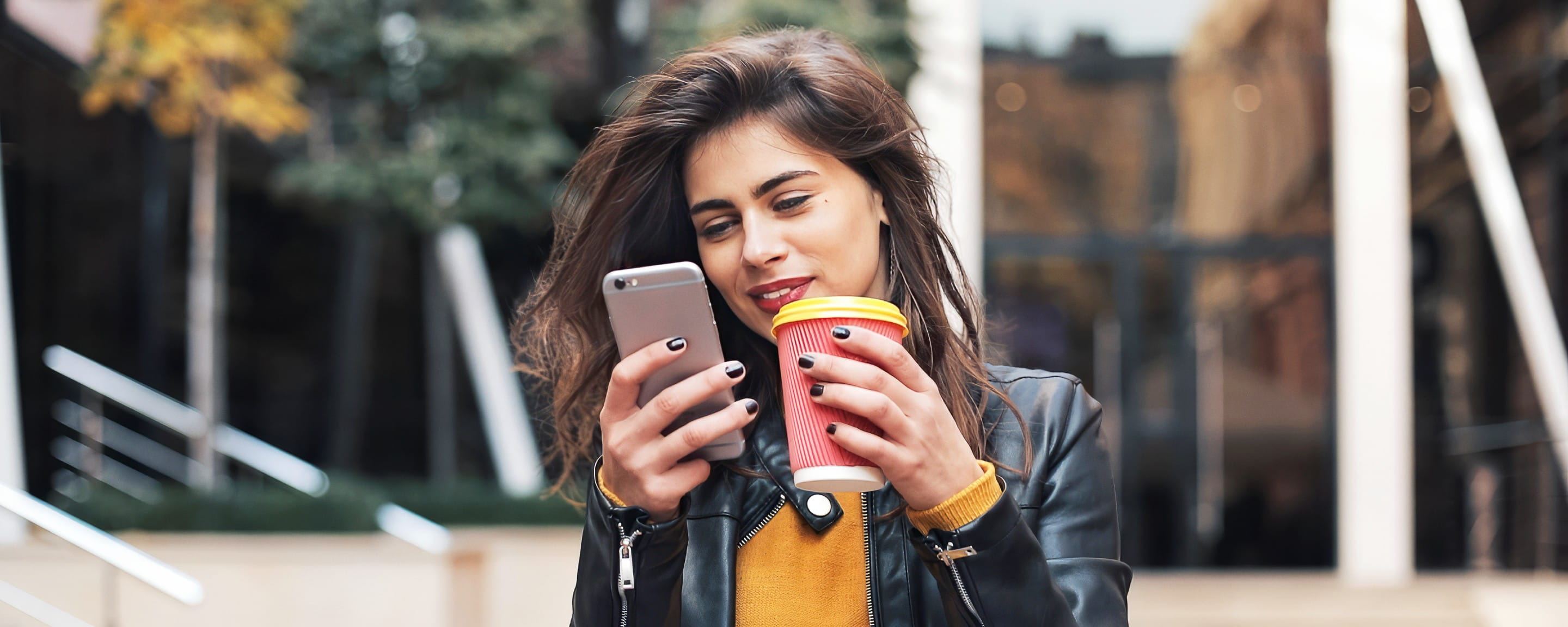 Young woman holds coffee and looks into mobile phone