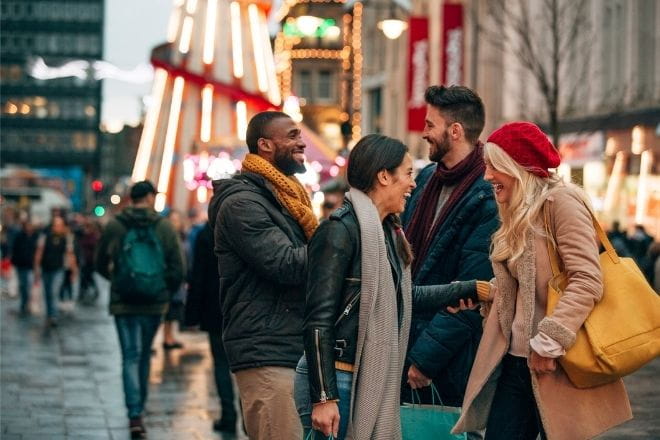 two couples laughing in the foreground with a Christmas fair in the background