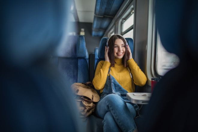 a woman wearing a yellow jumper listening to music on a train