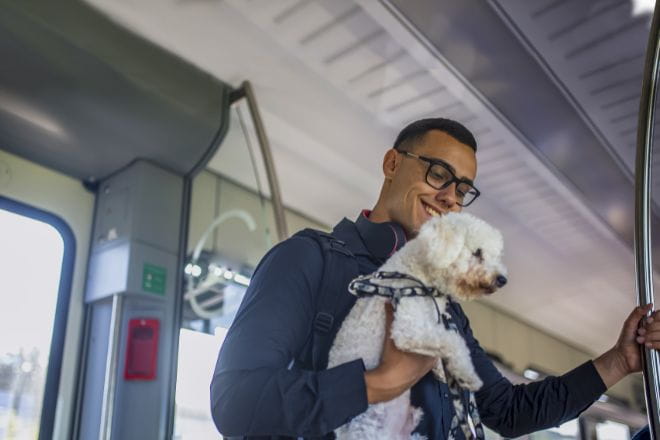 a man stood on a train holding a dog