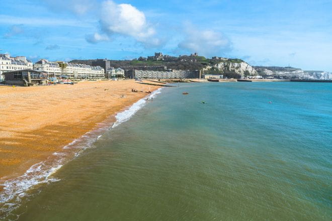 Dover Harbour beach on a sunny day with Dover Castle in the distance