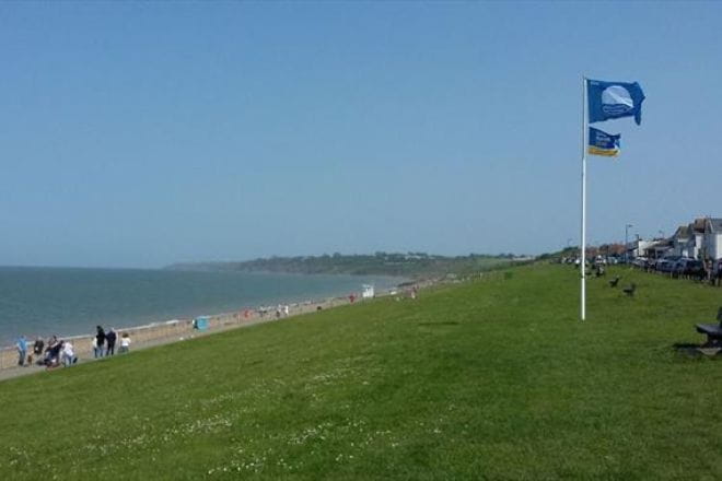 Minster Leas beach with a grassy bank to the right that has a flag on a pole blowing in the wind