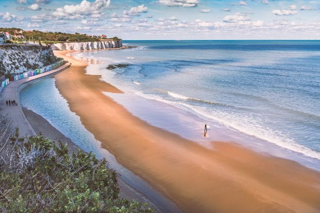 landscape of a beach and the ocean with white cliffs and a row of colourful huts in the background