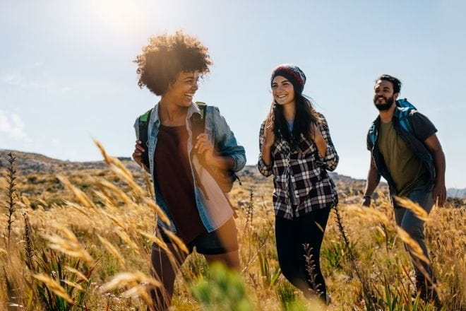 three friends walking through a field on a sunny day
