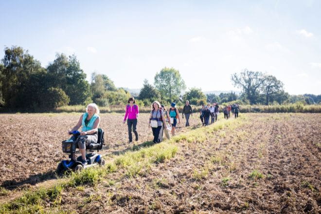 a group of people including one person in a wheelchair walking through the countryside