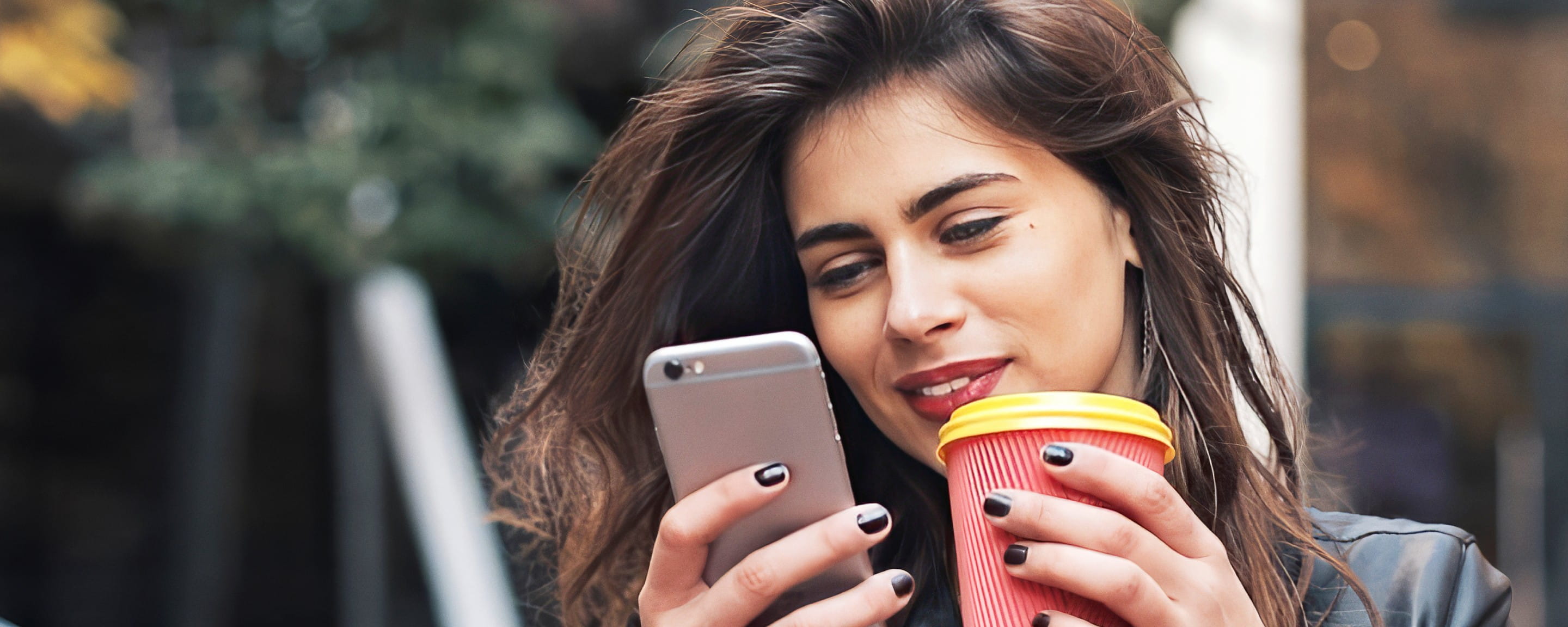Young woman holds coffee and looks into mobile phone