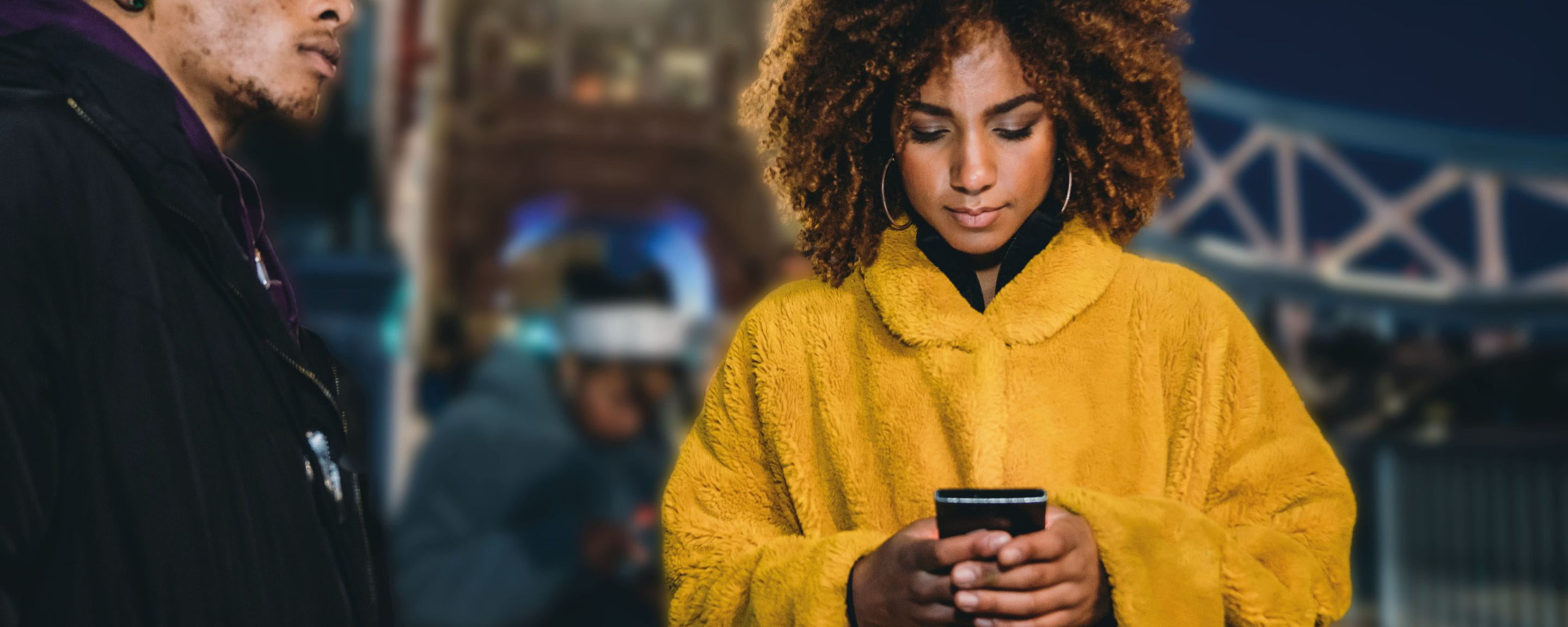 woman in yellow coat looking down at her phone