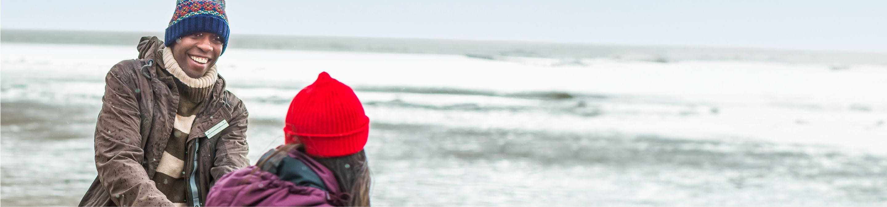 a couple holding wearing wooly hats, walking on the beach 