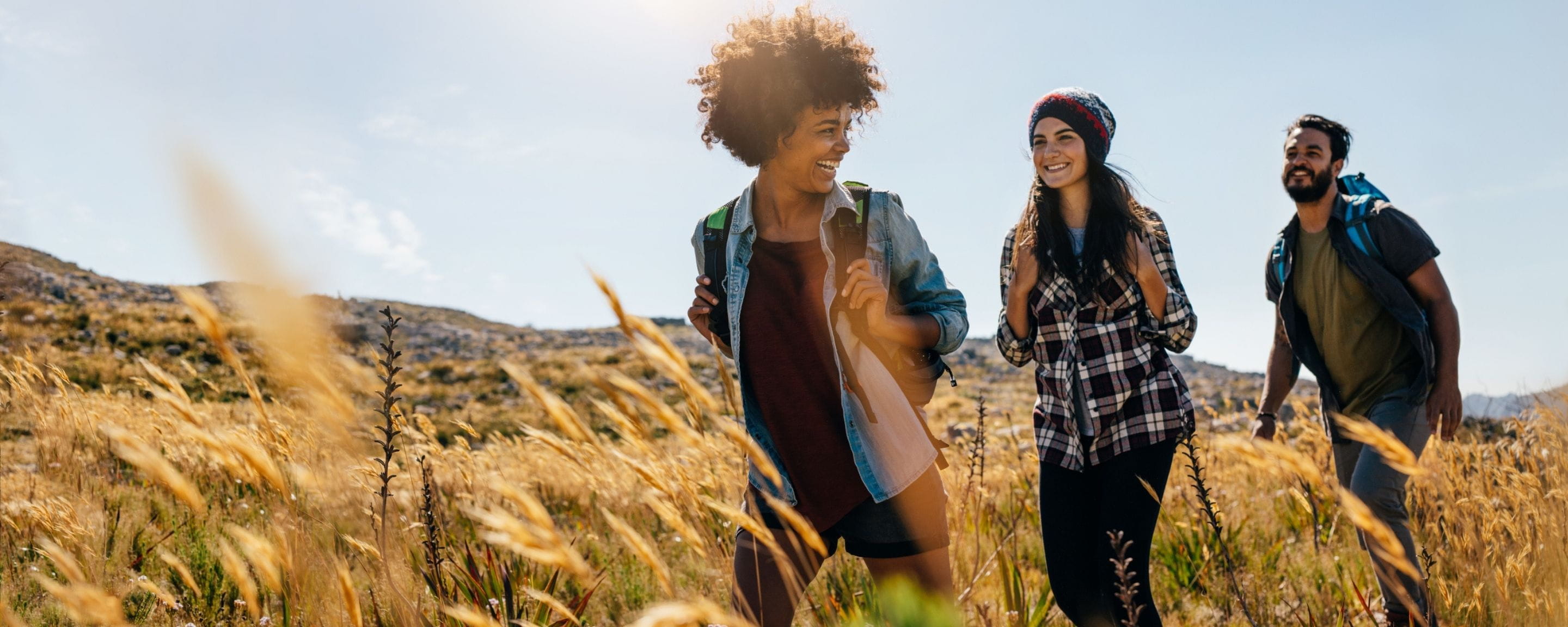 three friends walking through a field on a sunny day