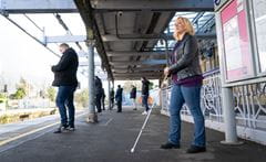 a woman with blind stick waiting on a platform