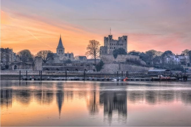 a sunset over a body of water with Rochester cathedral in the background