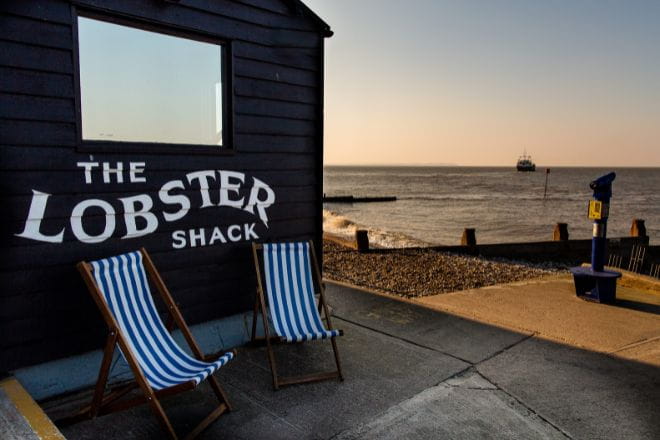 The Lobster Shack with two striped deck chairs in front and a view of the sea in the background