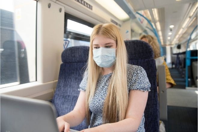 a woman wearing a mask using her laptop on a train