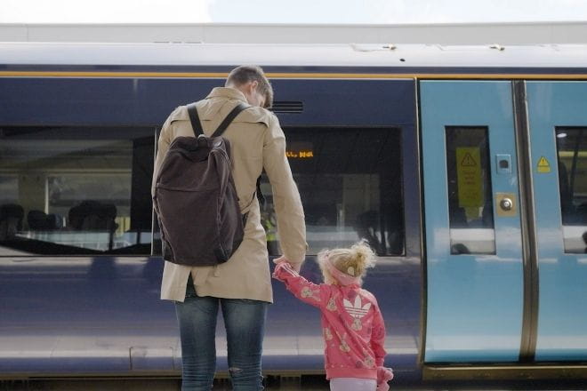 a man holding his child's hand on the platform as the train stops
