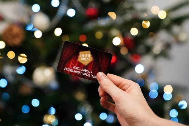a hand holding a theatre voucher with a blurry Christmas tree in the background