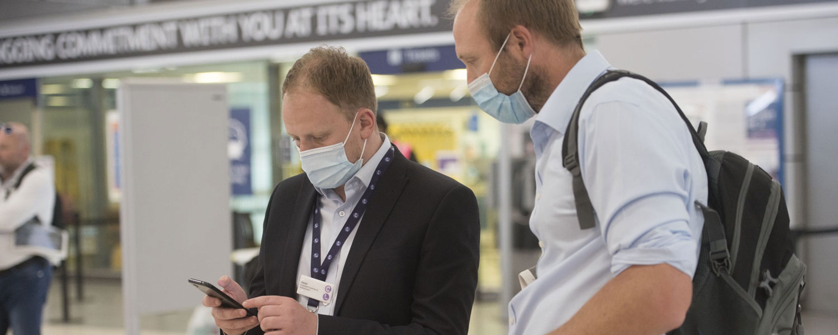 Two men wearing face masks checking a mobile phone