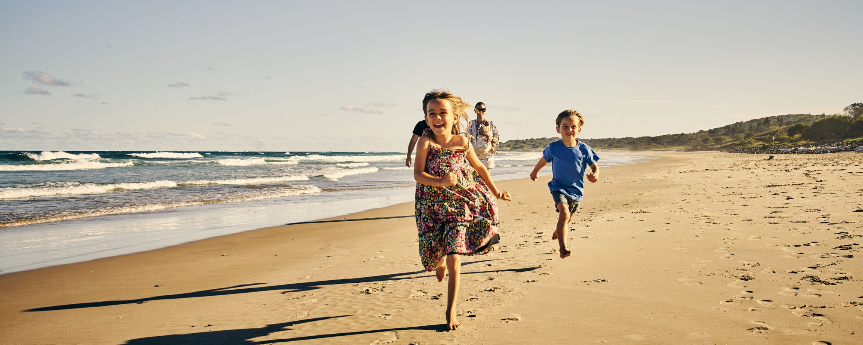 kids running on a beach with their parents behind