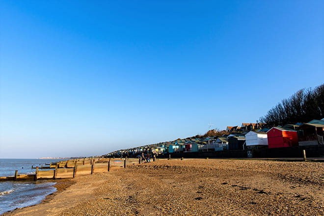 a beach in Whitstable with huts and blue sky in the background