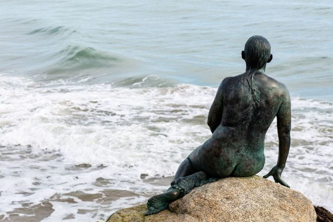 a statue sitting on a rock near the ocean